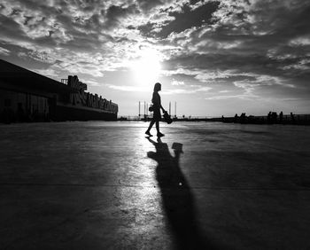 Silhouette woman walking in city against sky during sunset