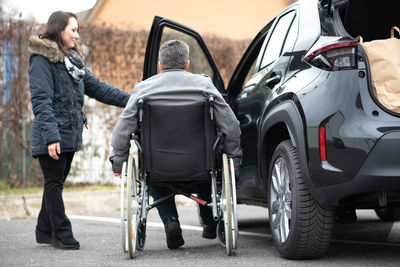 A woman helps aphysical disabled person to get into the car.