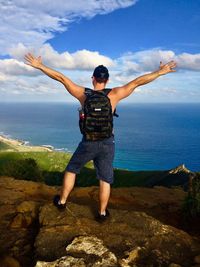 Rear view of man on rock at sea shore against sky