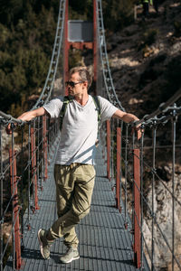 Man hiking in the mountains with backpack, standing on the bridge on sunny day.