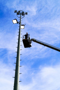 Low angle view of man on cherry picker by floodlight against sky