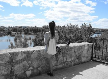 Rear view of woman standing by retaining wall against sky