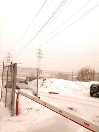 Electricity pylon on snow covered field against sky