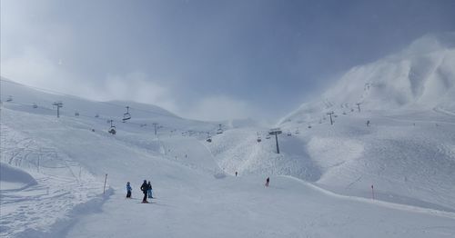 Low angle view of people skiing on snowcapped mountain against sky