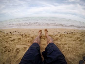 Low section of man resting at beach against sky