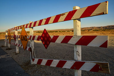 End of paved road barrier with red and white stripes and reflectors and signs in desert