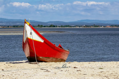 Red boat moored on beach against sky