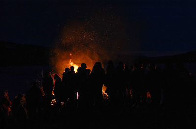 Silhouette people by bonfire against sky at night