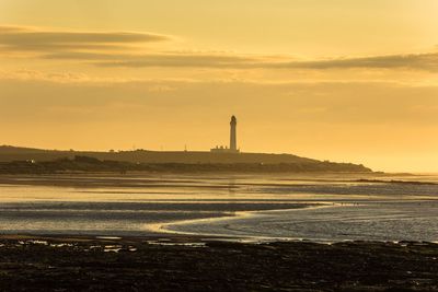 Lighthouse by sea against sky during sunset