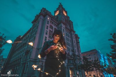 Low angle view of woman standing against illuminated buildings in city