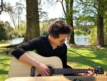 Young man playing guitar sitting in park