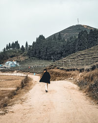 Rear view of man walking on street amidst buildings against sky