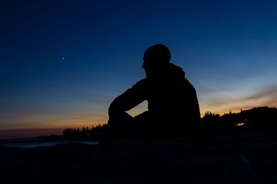 Silhouette man sitting against blue sky during sunset