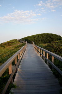 Footbridge leading towards dunes against sky