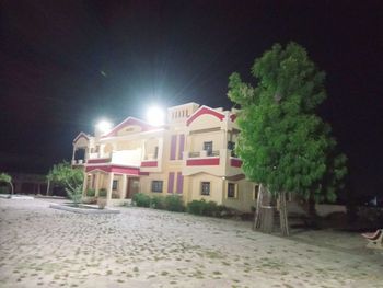 Illuminated street by buildings against sky at night