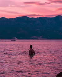 Rear view of shirtless man in sea against sky during sunset