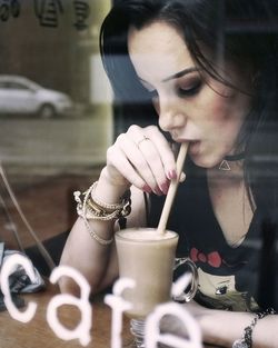 Woman drinking coffee in cafe seen through window