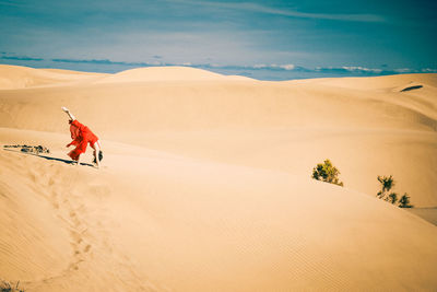 Side view of mature woman dancing on sand at desert against sky