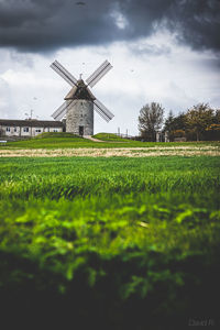 Windmill on field against cloudy sky
