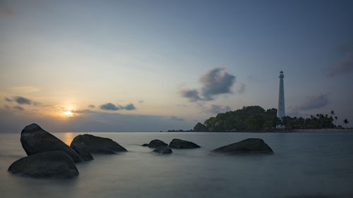 Rocks in sea against sky during sunset