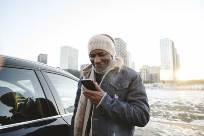 Smiling man using smart phone outside car in winter