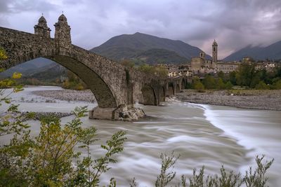 Arch bridge over river against cloudy sky