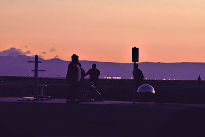 Silhouette people standing against orange sky during sunset