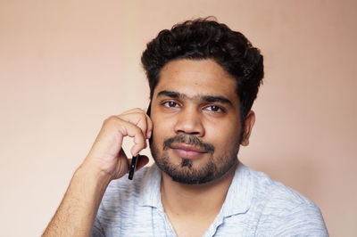 Close-up portrait of young man talking on mobile phone against wall