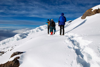 Rear view of people climbing snow covered mountain