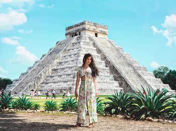 Low angle view of woman standing by building against sky