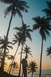 Silhouette woman standing by palm trees at beach during sunset