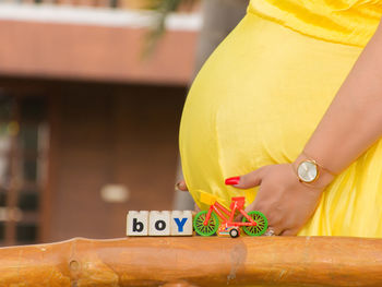 Midsection of pregnant woman standing by toy bicycle and text