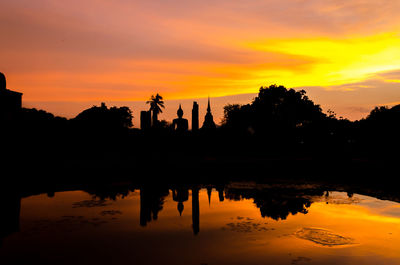 Silhouette trees by lake against orange sky