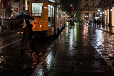 People walking on wet illuminated city at night