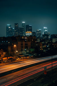 Light trails on road against illuminated buildings in city at night