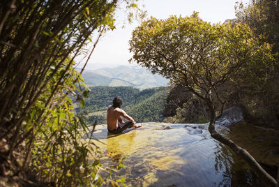 Shirtless man sitting on looking at view while sitting on mountain