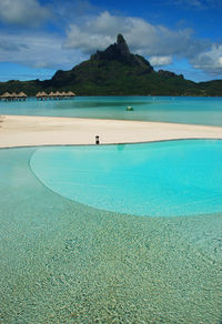 Infinity pool at beach by mountain against sky