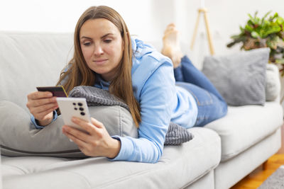 Portrait of young woman using mobile phone while sitting on sofa at home