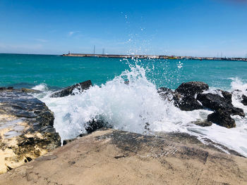 Waves splashing on rocks at shore against sky