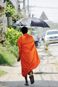 Rear view of monk walking on road in city