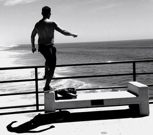 Full length of shirtless man standing on sea shore against sky