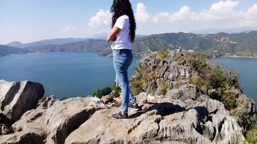 Low section of young woman standing on rock by lake