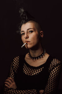 Portrait of young woman smoking over black background