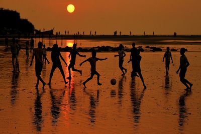 Silhouette people playing on beach against sky during sunset