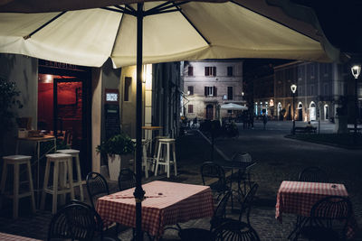 Empty chairs and tables at sidewalk cafe in city