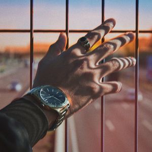 Cropped hand of man with wristwatch touching metal grate against highway