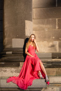 Full length portrait of young woman in pink evening gown sitting against columns