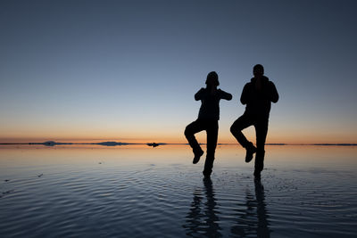 Silhouette people on sea against clear sky during sunset