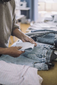 Male fashion designer folding fabric with jeans on workbench at workshop