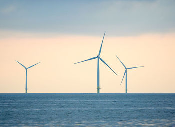 Wind turbines in sea against sky during sunset